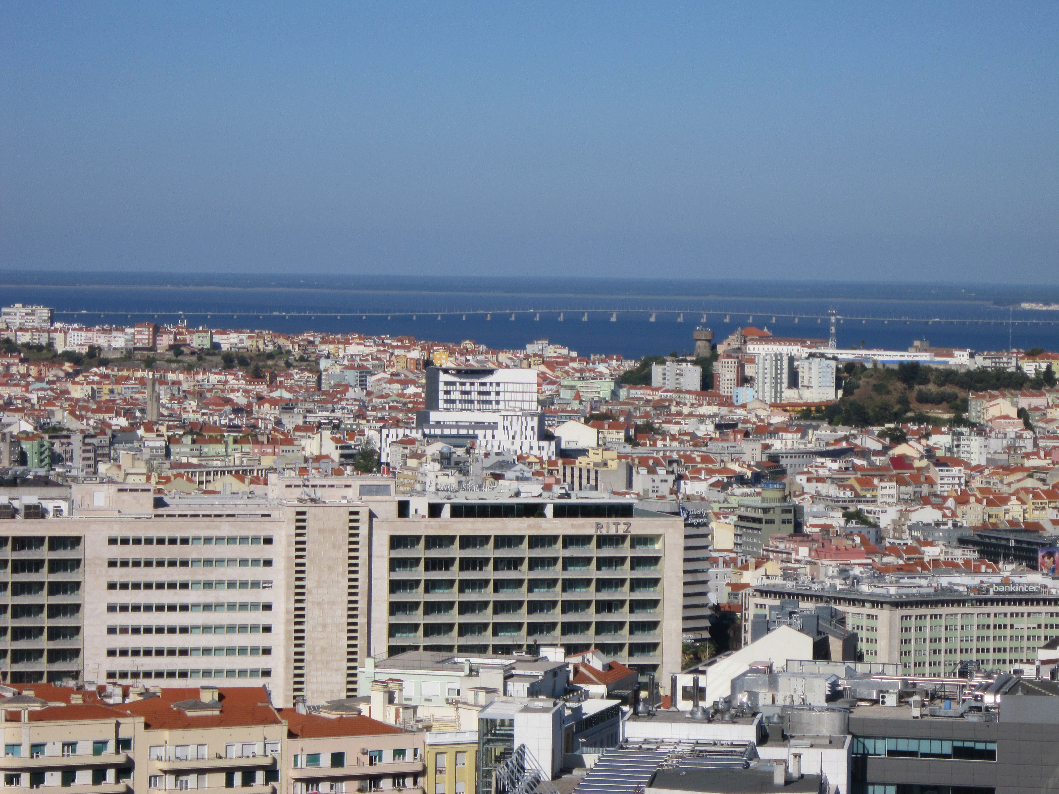 Aerial view of Lisbon, Portugal with modern urban buildings, rooftops and the Tagus River bridge in the background