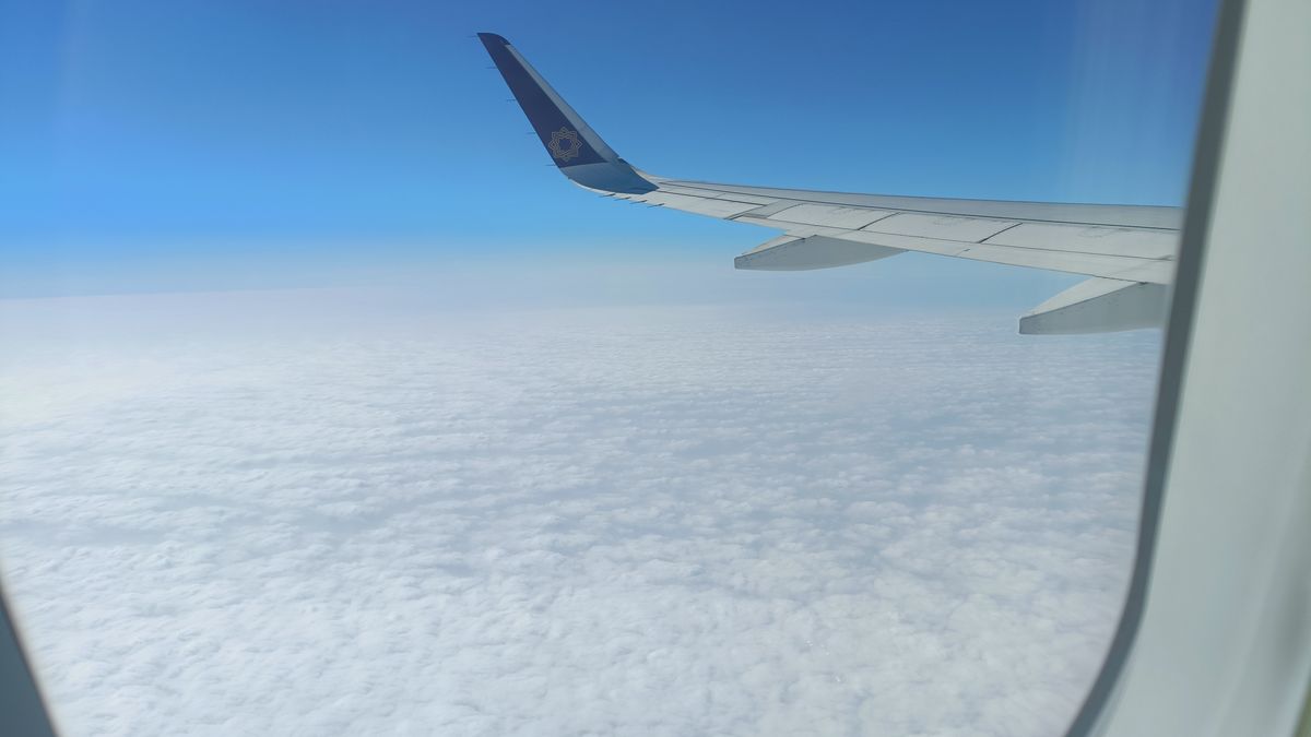 View of an airplane wing above clouds under a clear blue sky, captured from a window seat.