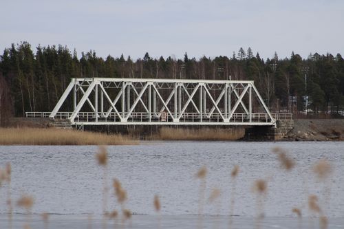 Free Metal bridge spans across a tranquil river in Finland, surrounded by autumn trees. Stock Photo