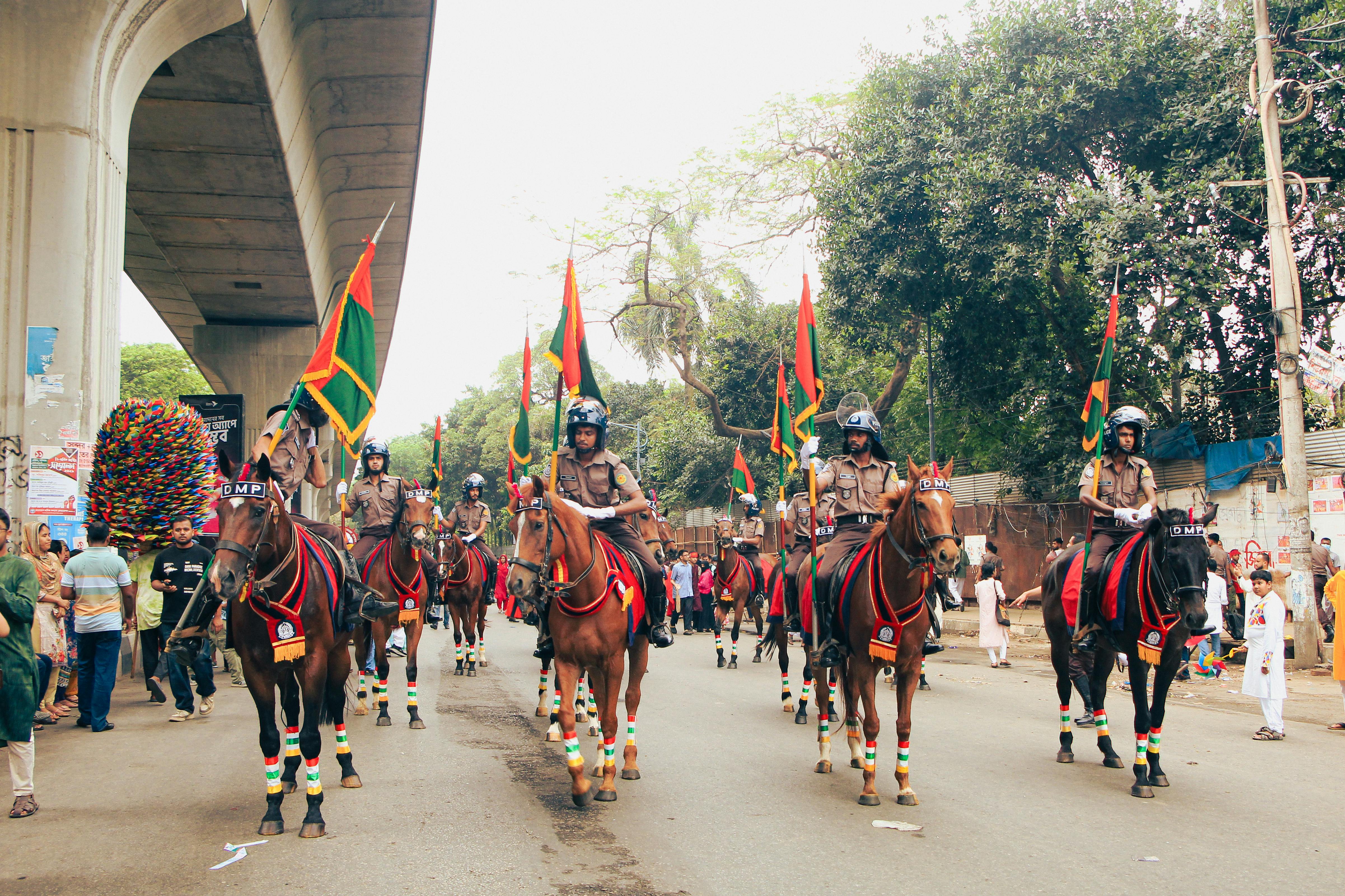A vibrant parade in Dhaka featuring horses and colorful flags during a cultural festival.