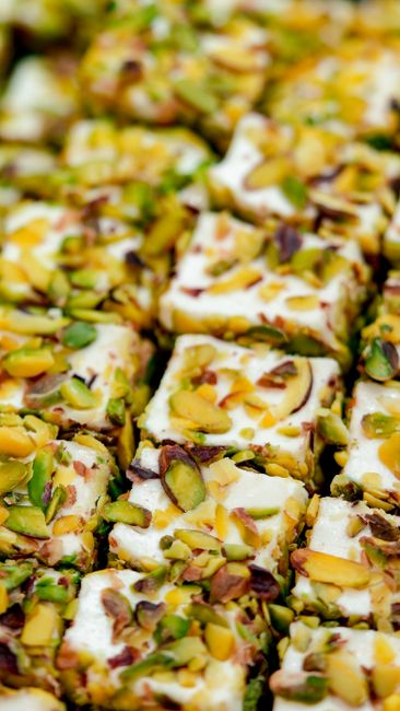 A block of pale nougat studded with whole almonds and pistachios, sliced to show its chewy, aerated interior.