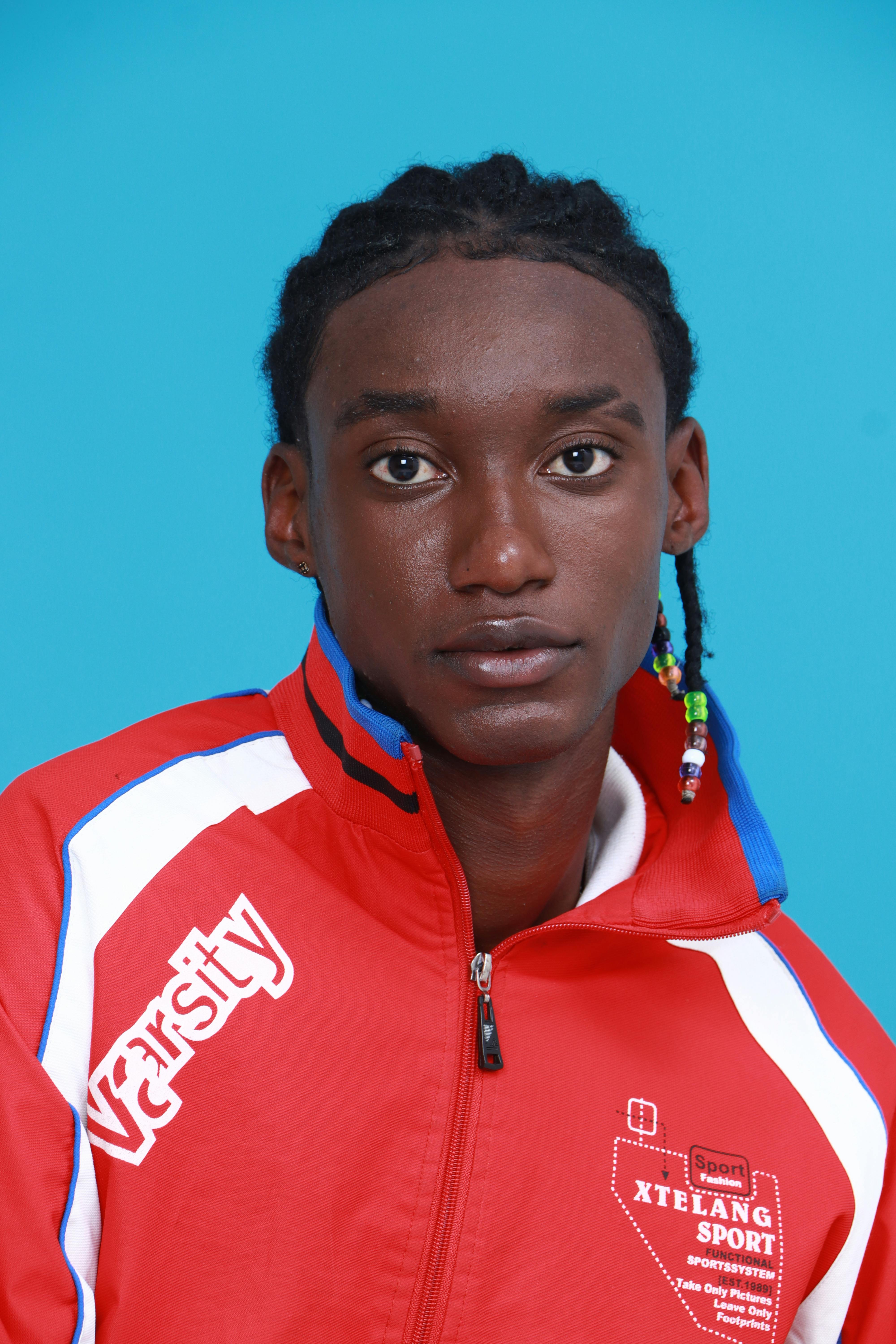 Studio portrait of a confident young adult wearing a vibrant red sports jacket against a blue background.