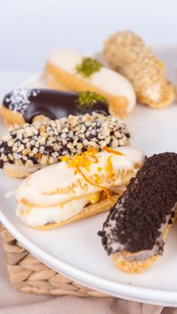 Close-up of assorted gourmet eclairs topped with various ingredients on a white plate.
