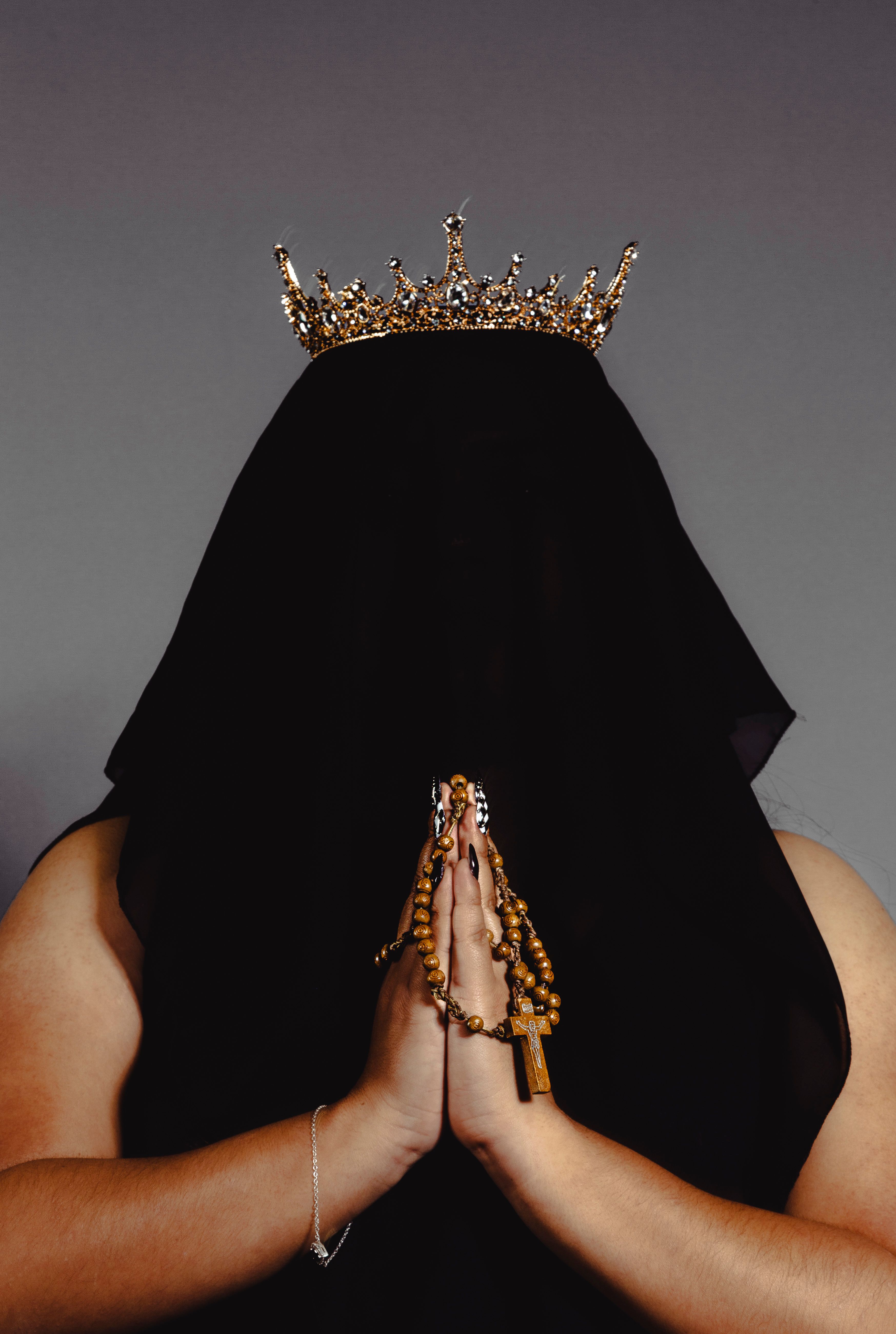 Veiled figure with crown and prayer beads in contemplative pose.
