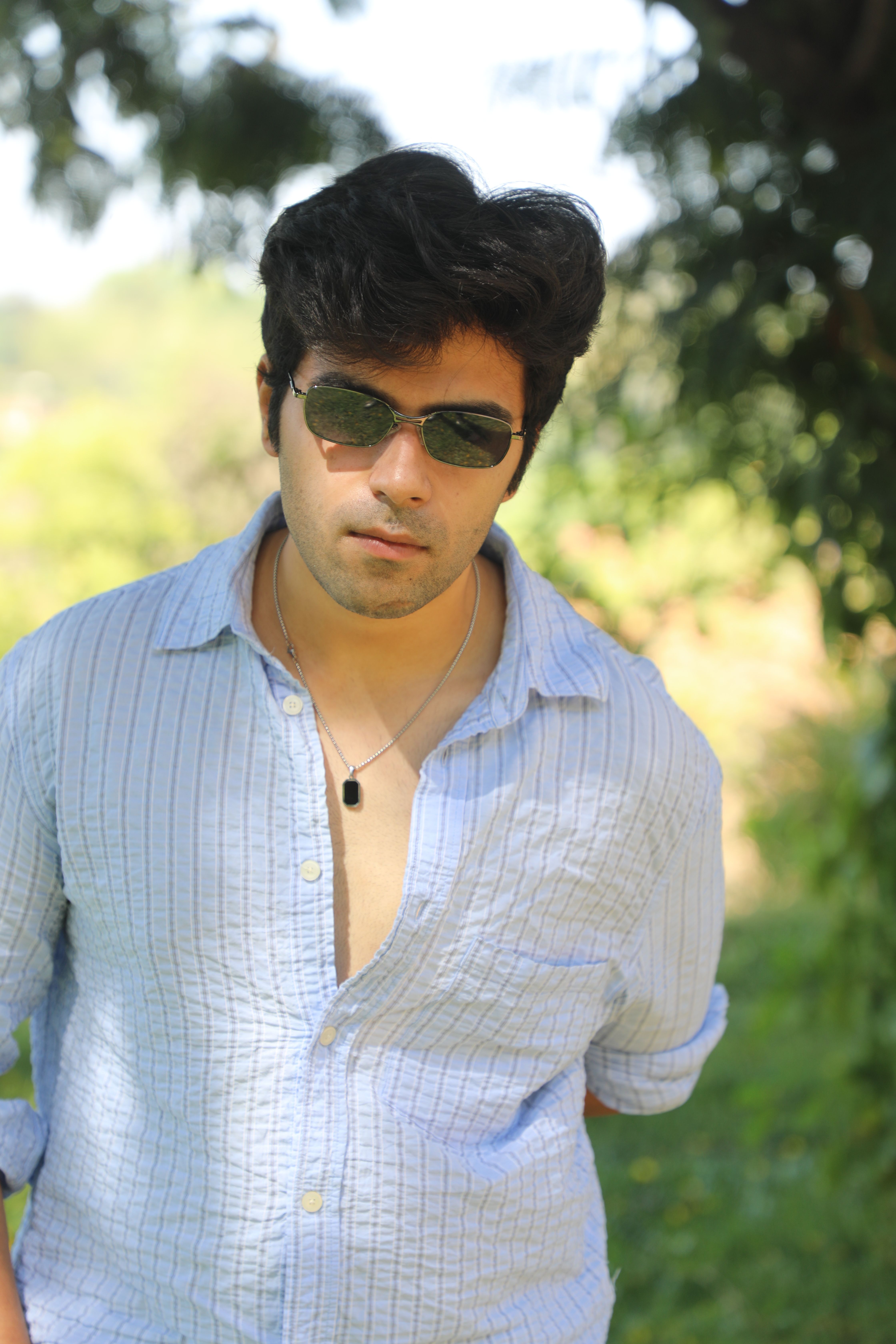Young man in sunglasses poses casually outdoors, exuding confidence.