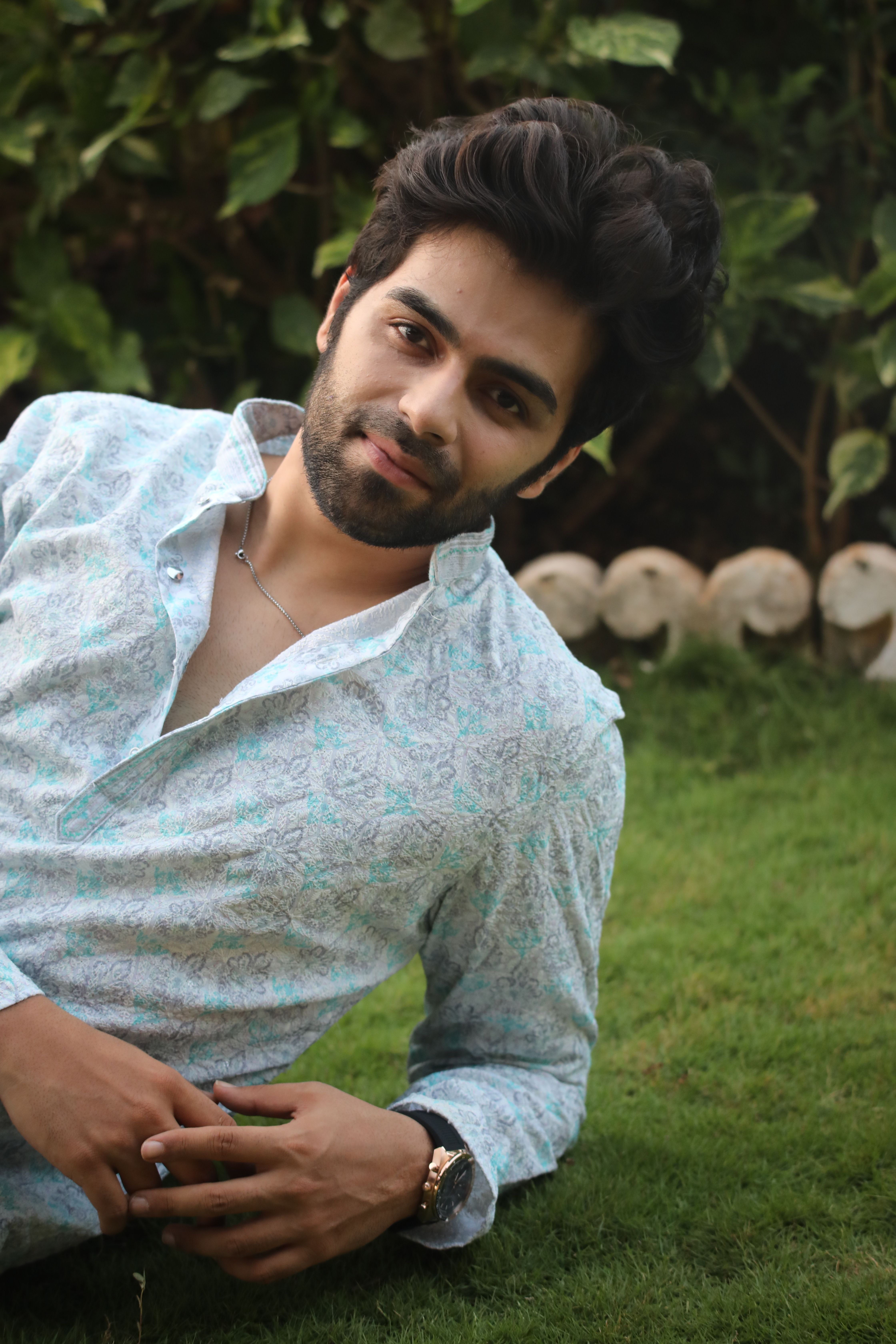Young man in floral shirt lying on grass, smiling outdoors.