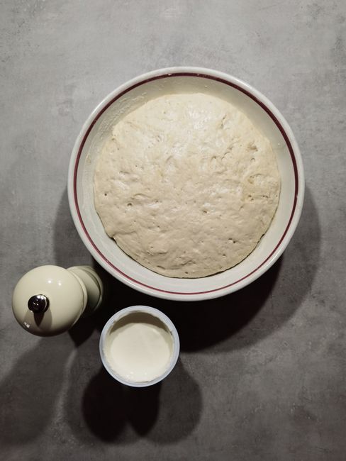 A glass bowl of self rising flour with a whisk resting on top, next to a measuring cup of all-purpose flour and small dishes of baking powder and salt.