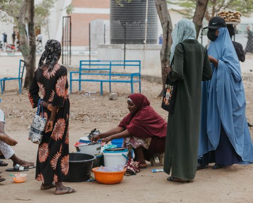 Free A group of women engage with a street vendor selling goods in an outdoor market setting. Stock Photo