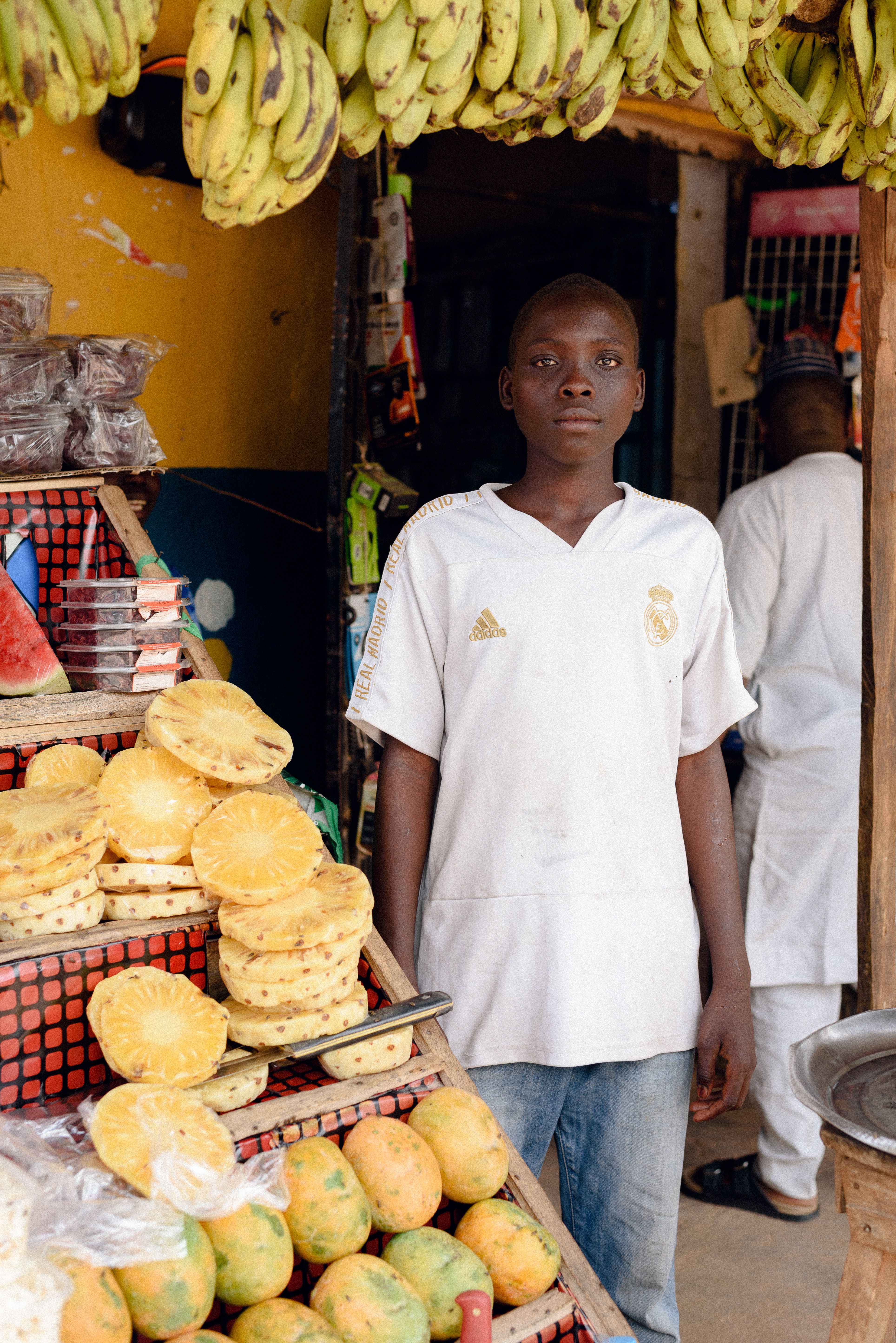Un adolescent vend des ananas et des bananes sur son étal de marché
