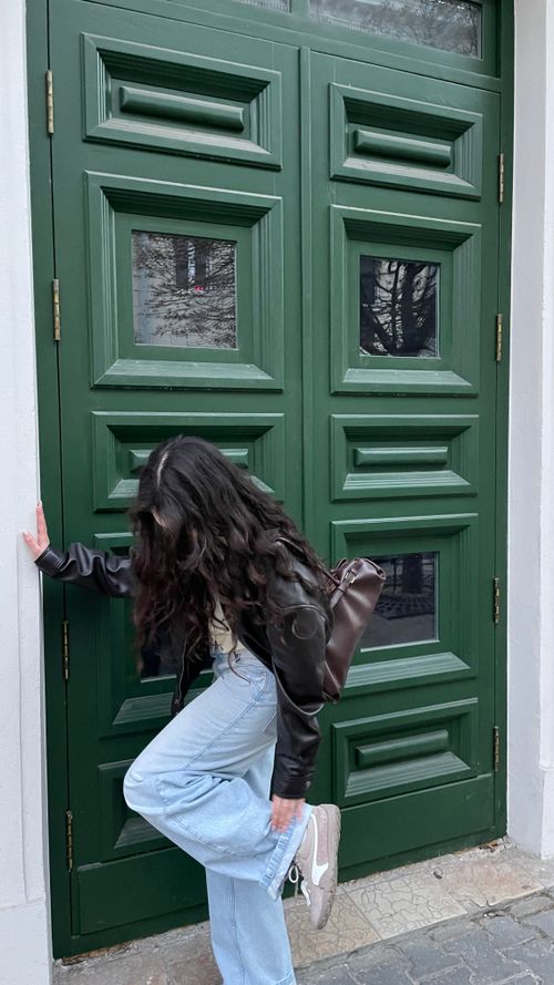 Free Stylish woman posing near an ornate green door in urban setting. Stock Photo
