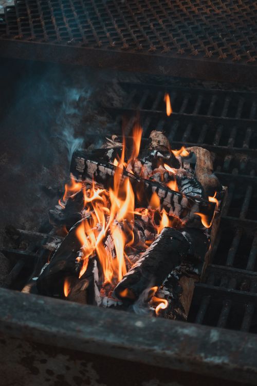 Free Close-up of a cozy campfire with wood and flames in a grill setting, perfect for outdoor gatherings. Stock Photo