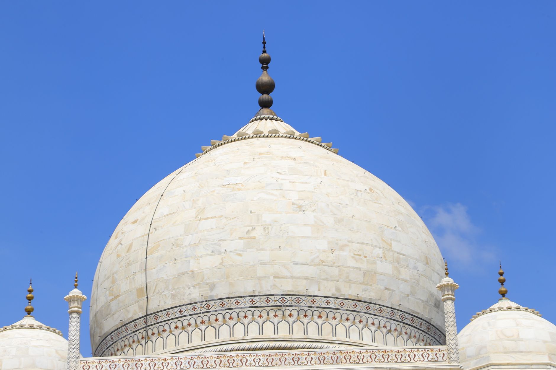 Close-up of the iconic marble dome of the Taj Mahal against a bright blue sky.