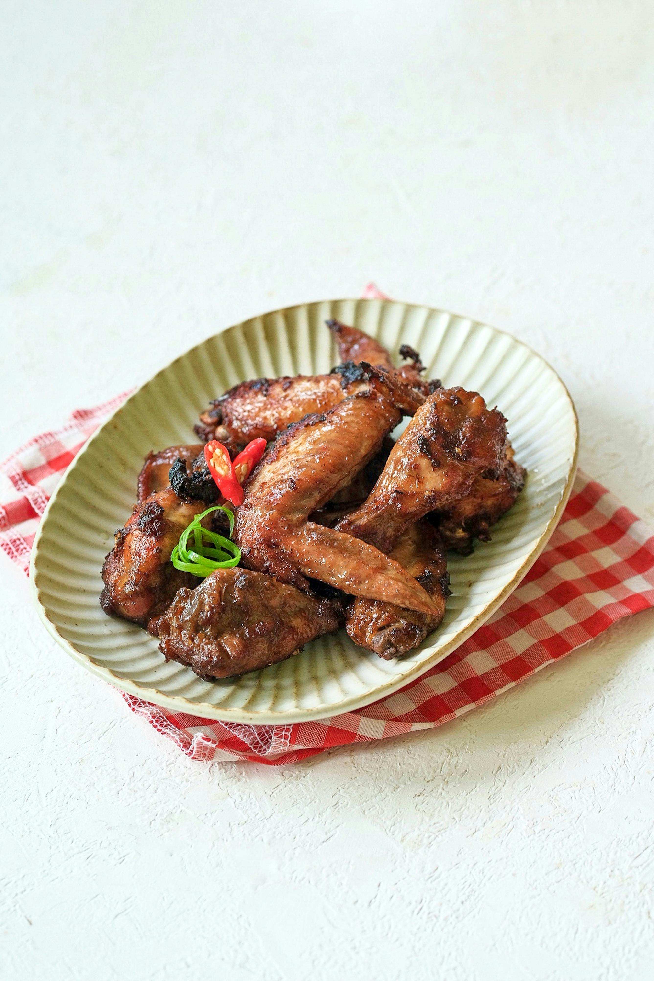 Golden crispy chicken wings coated in a glossy dark reddish-brown Thai chili glaze, garnished with fresh cilantro leaves and thin slices of red Thai chilies