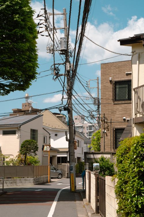 Free Calm residential street in Tokyo featuring utility poles and traditional Japanese houses under a blue sky. Stock Photo
