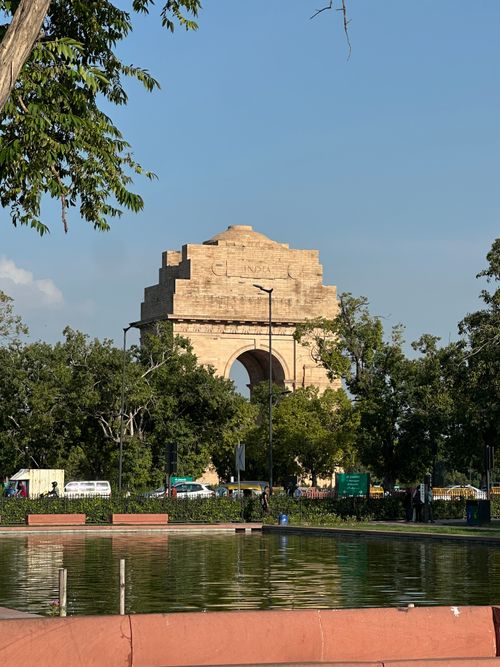 Free View of the historic India Gate in New Delhi, surrounded by greenery and reflected in nearby water. Stock Photo