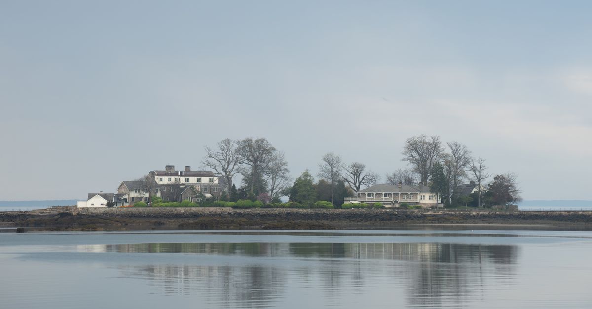 A serene view of a stately manor island reflecting in the calm waters on a clear day.