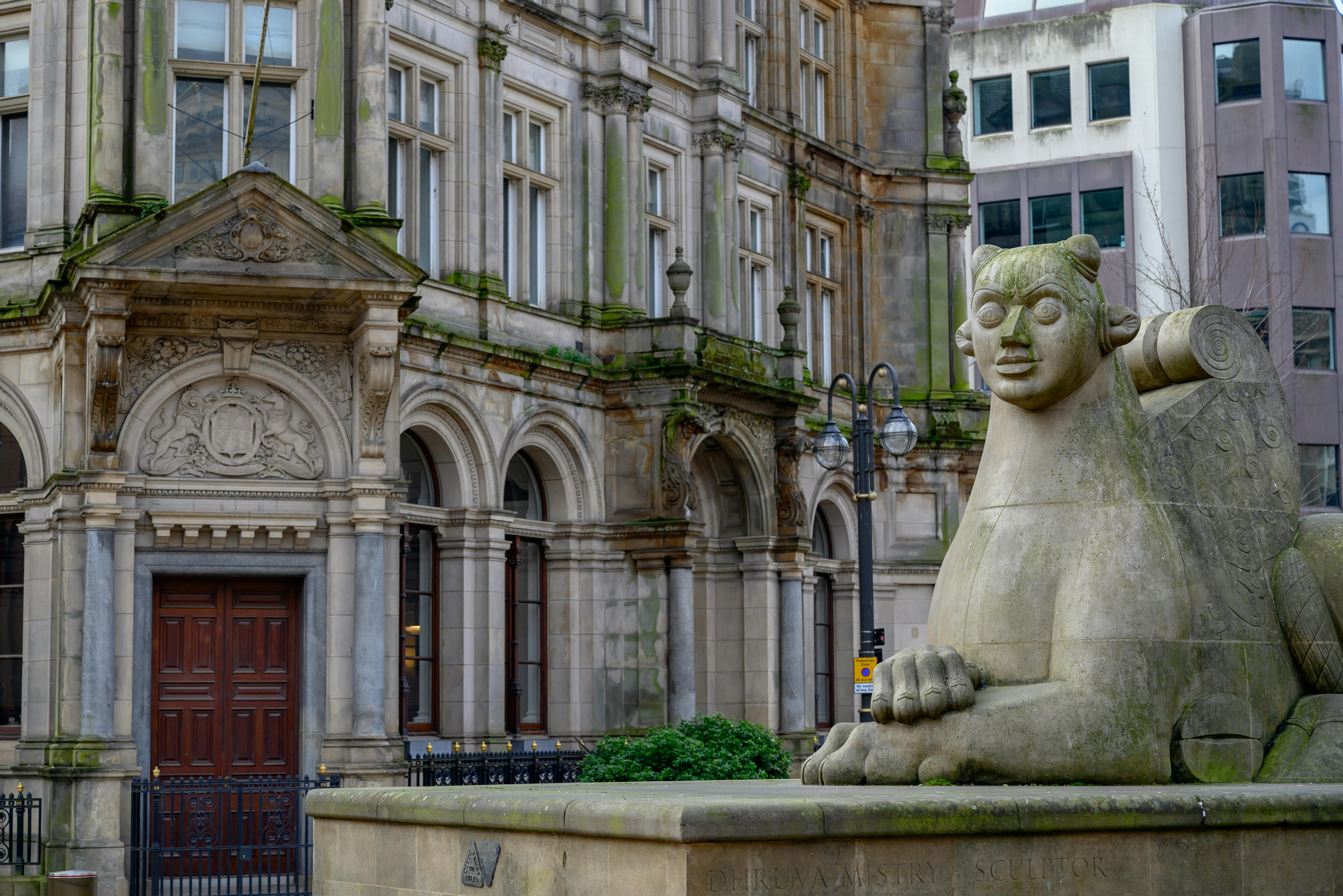 A grand historic building with intricate architectural details and a stone sphinx statue in the foreground in England.