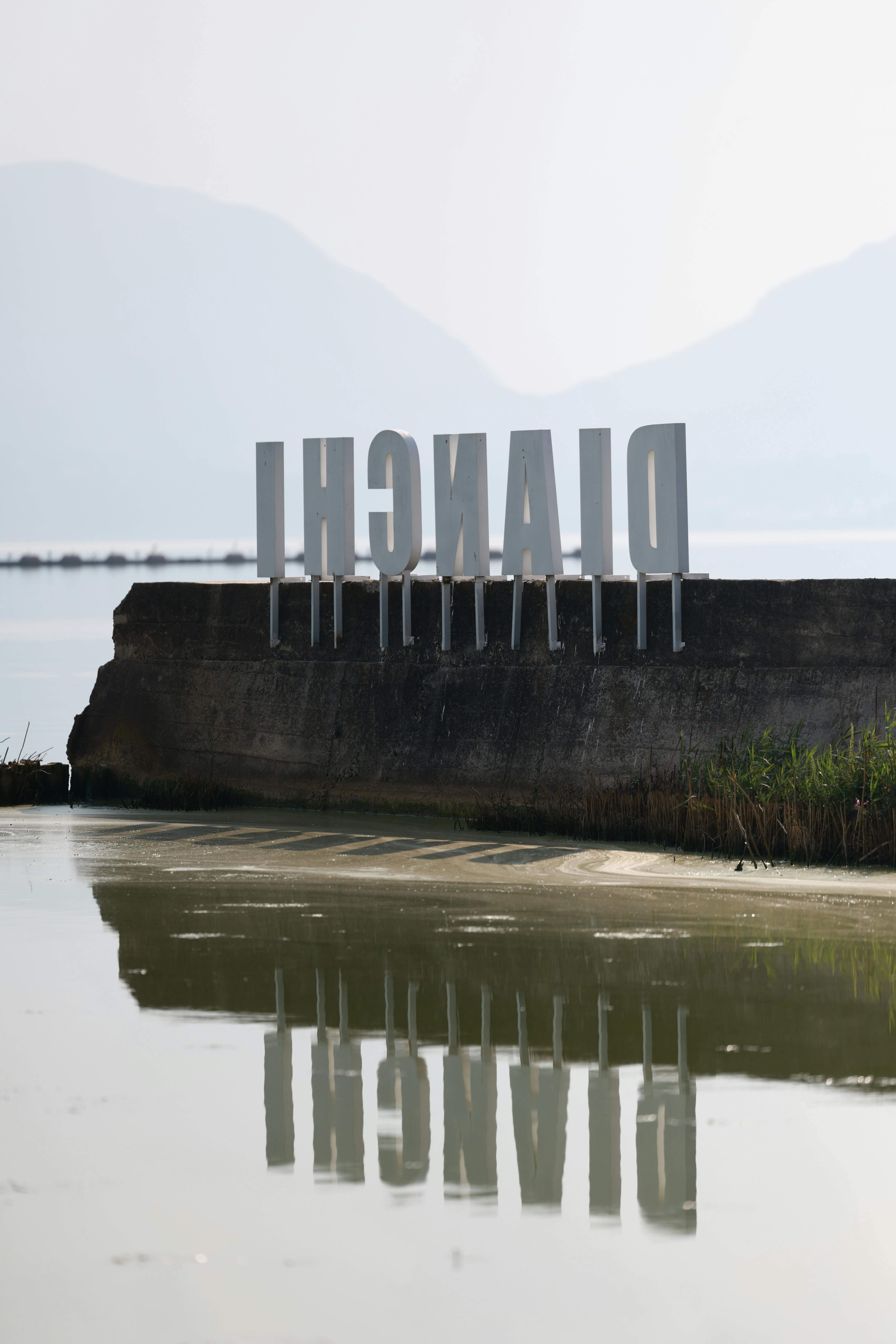 Serene outdoor scene featuring a Milano sign reflecting in water.