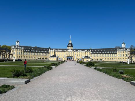 Front view of Karlsruhe Palace, Germany, with clear blue skies and a person walking in the foreground.