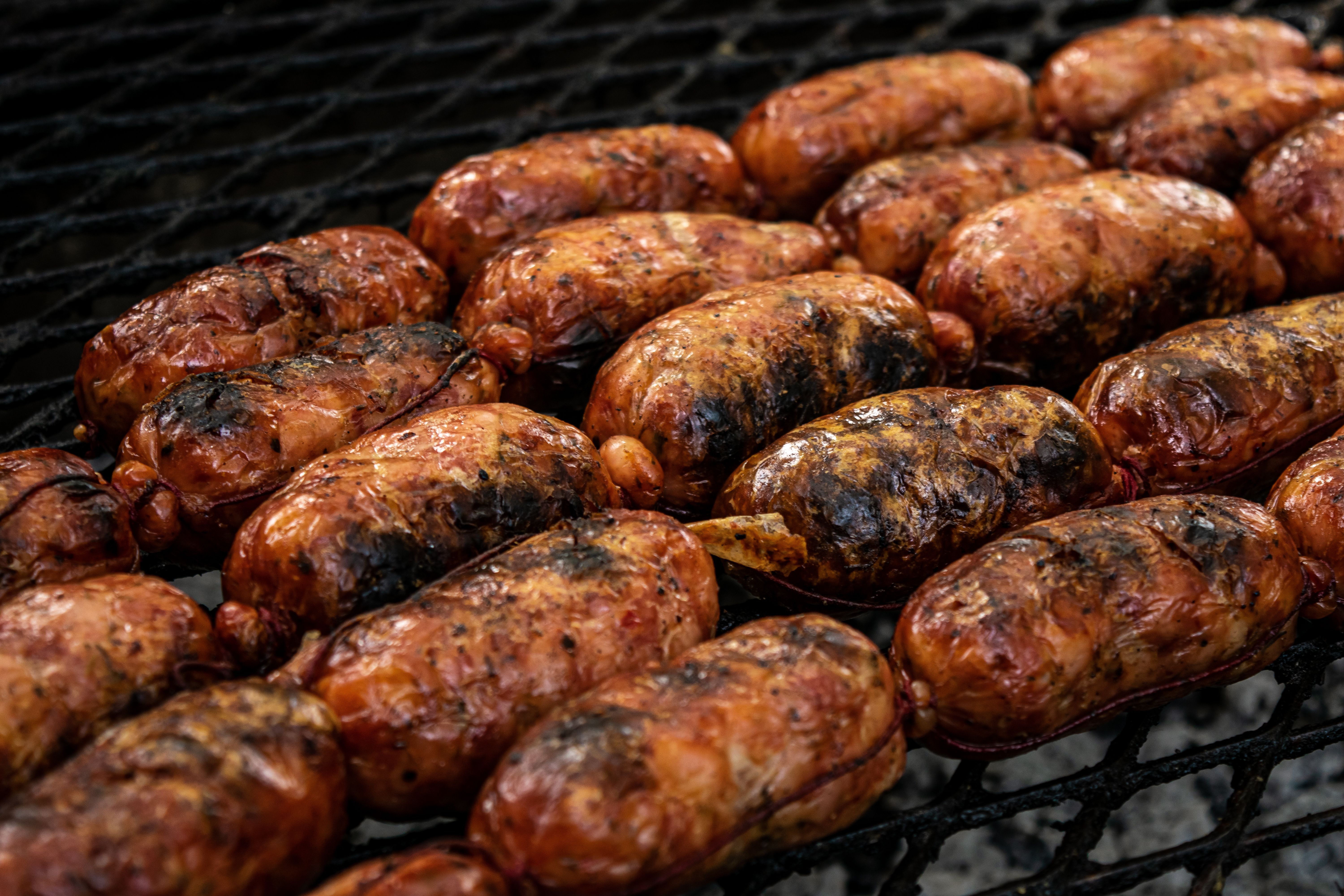 Gros plan sur de savoureuses saucisses grillées qui grésillent sur un barbecue.