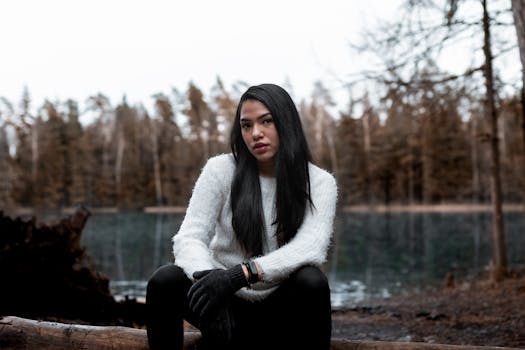 秋日里，一名身着舒适毛衣的女子，若有所思地坐在宁静的森林湖边