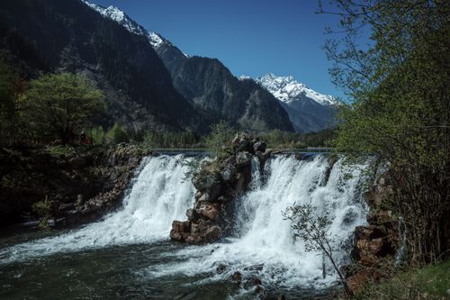 Free Stunning waterfall with snow-capped mountains in Sichuan, China, offers a serene natural landscape. Stock Photo