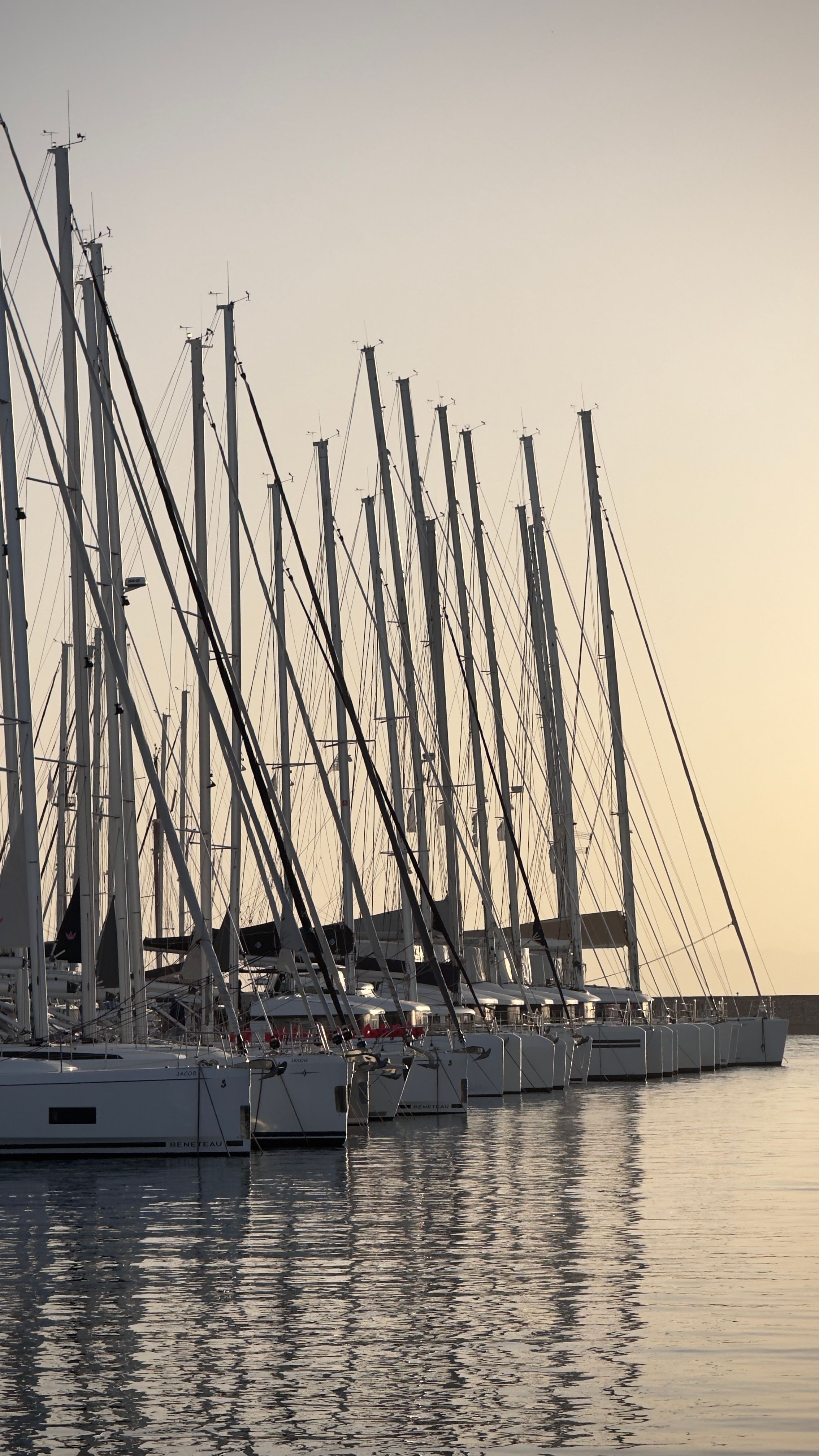 A serene view of sailboats docked at a marina during sunset in Greece, showcasing a calm seascape.