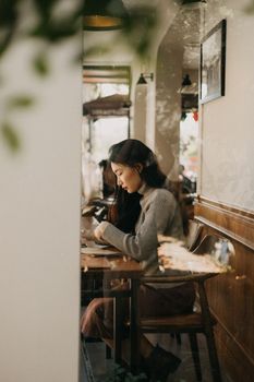 Woman in a cafe working, with reflections on the window, creating a soft, contemplative scene.