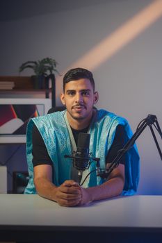 A young man in traditional attire podcasting from his modern home studio with soft lighting.