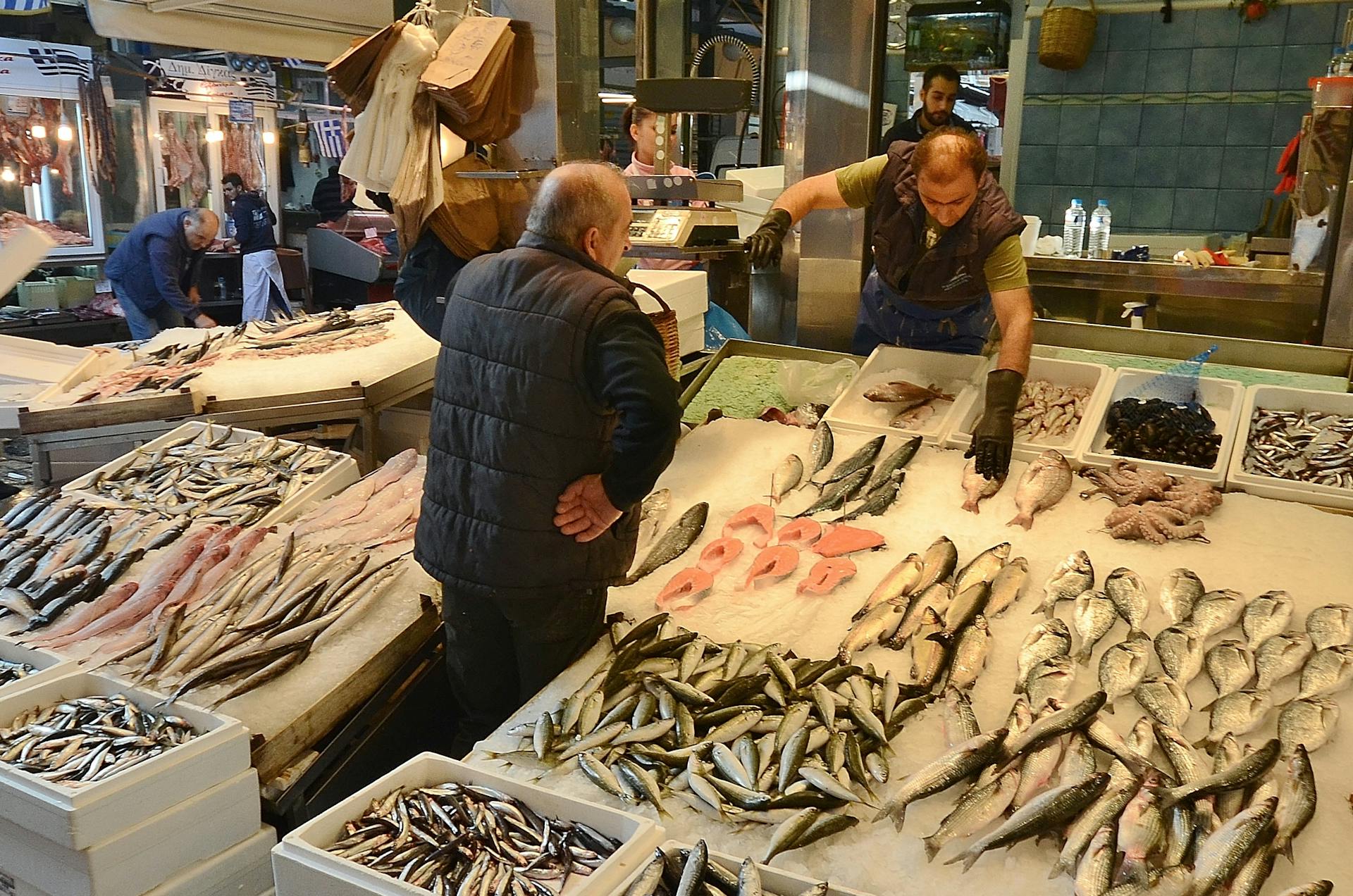 Fish market with vendors and fresh seafood display, bustling activity captured.