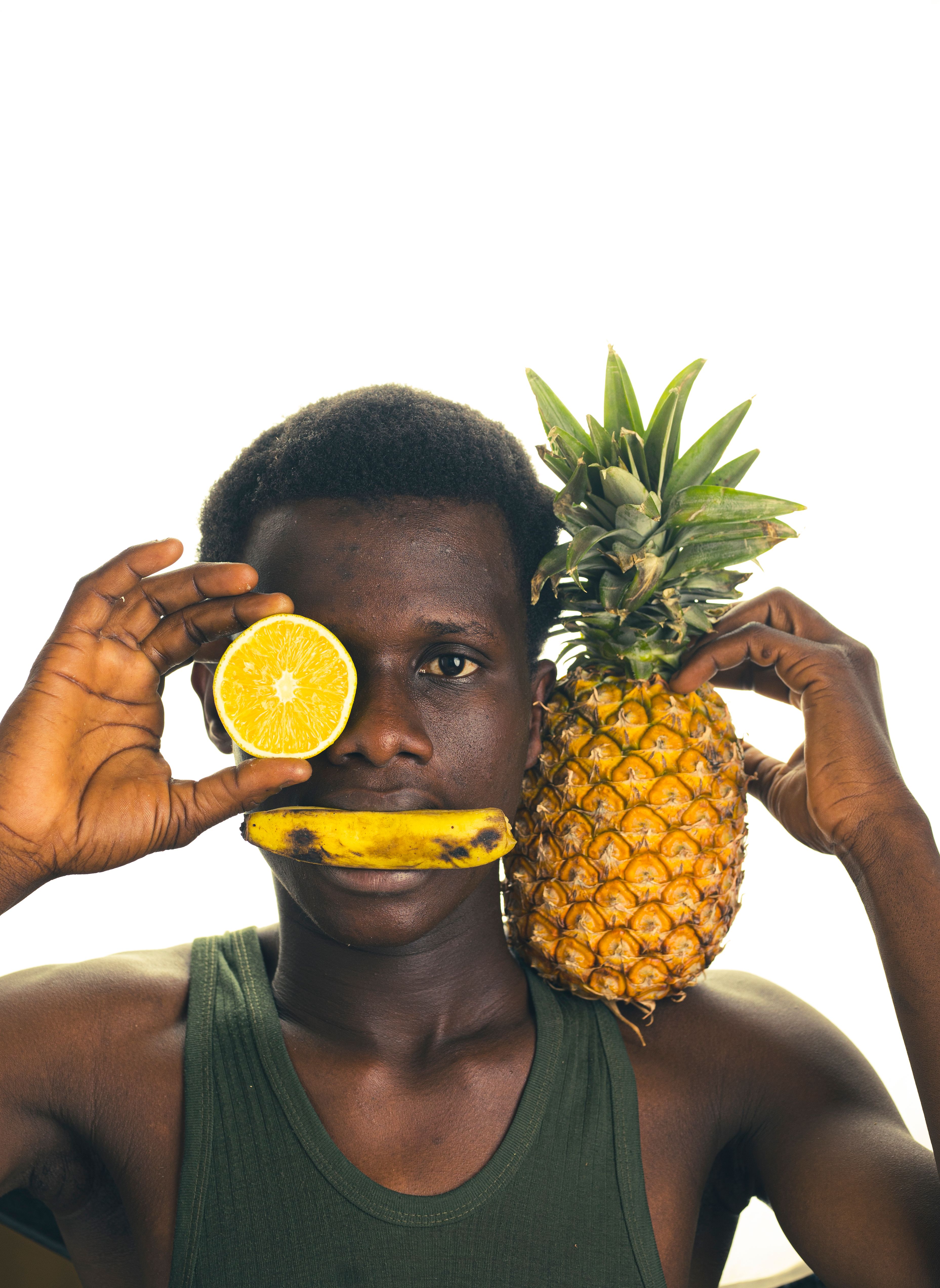 Vibrant portrait of a young man posing with orange slice, banana, and pineapple for a playful and colorful look.