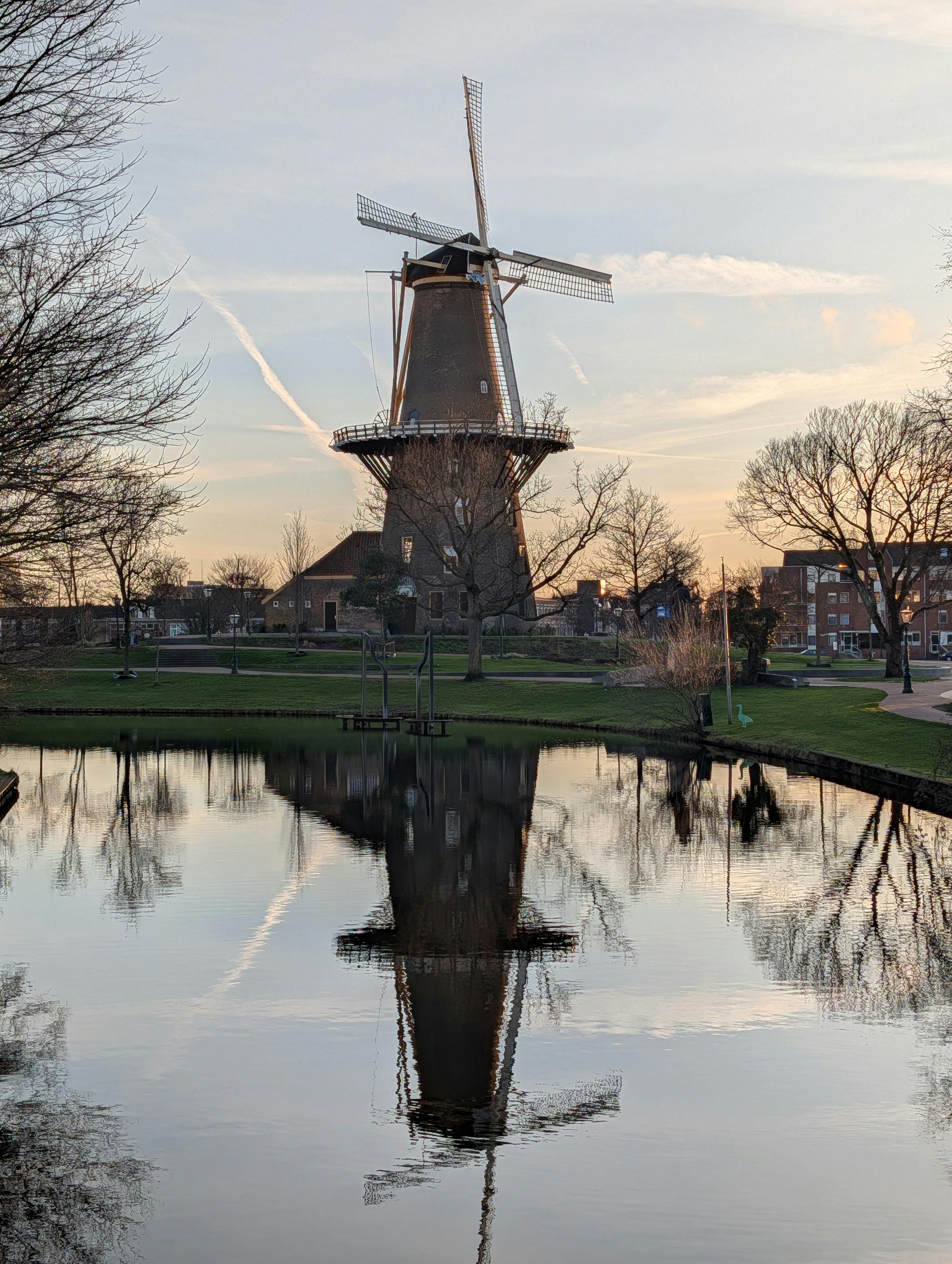 Picturesque windmill reflecting in a calm canal at sunset in Leiden, Netherlands.