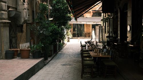 Free Cozy alleyway with outdoor cafe seating, lush greenery, and a solitary pedestrian. Stock Photo
