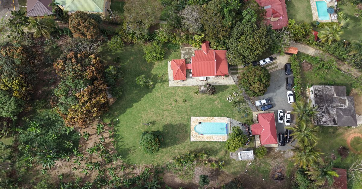 Bird's-eye view of a lush property with red-roofed buildings and swimming pools, surrounded by tropical greenery.