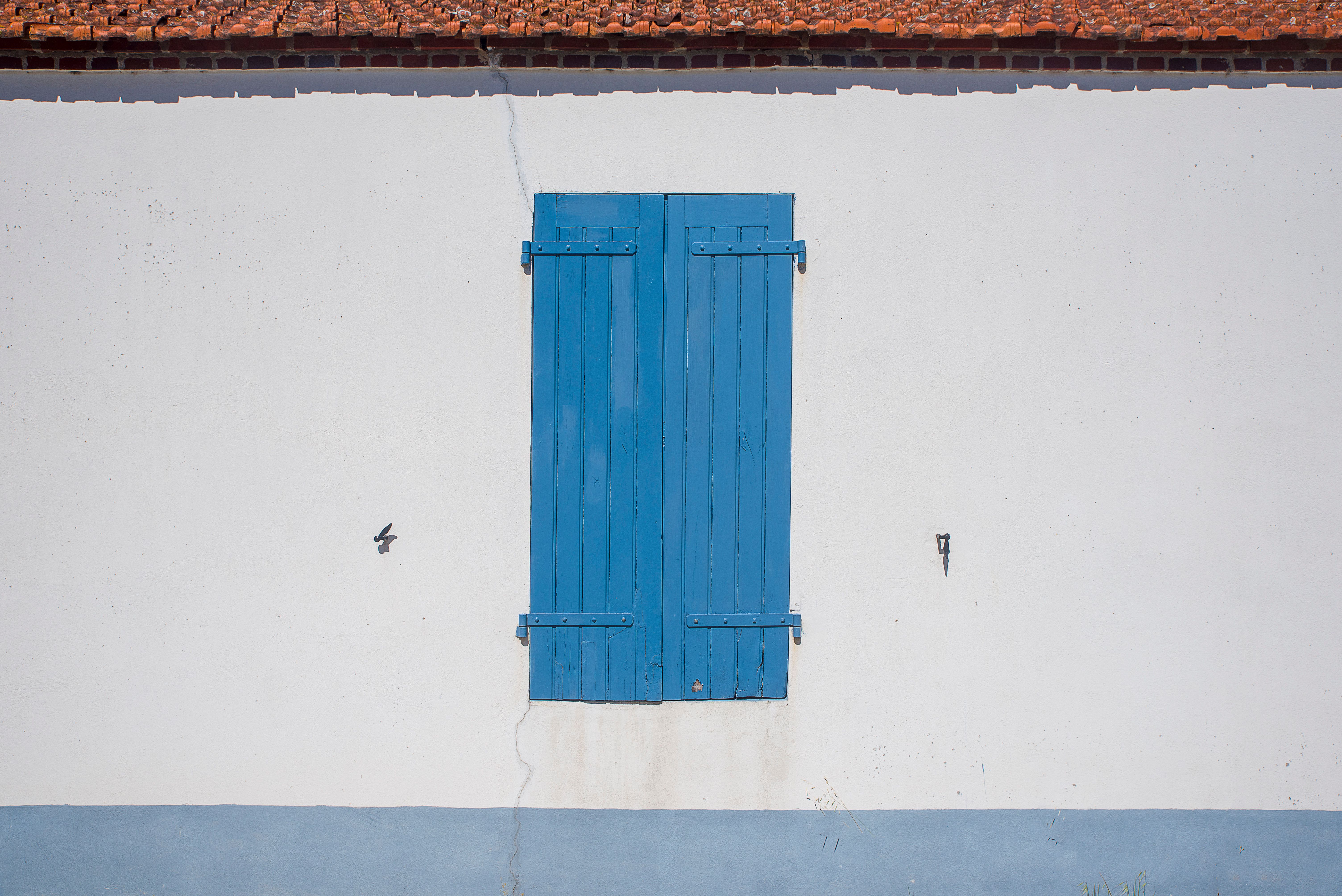 Simple minimalistic exterior with a closed blue shutter on a white wall and red roof.