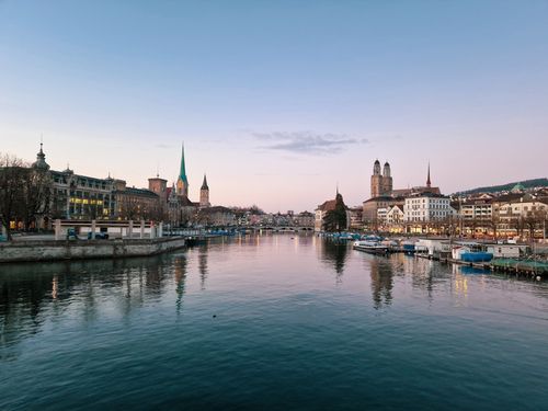 Free Beautiful evening view of Zürich's skyline with the river reflecting illuminated historic architecture. Stock Photo