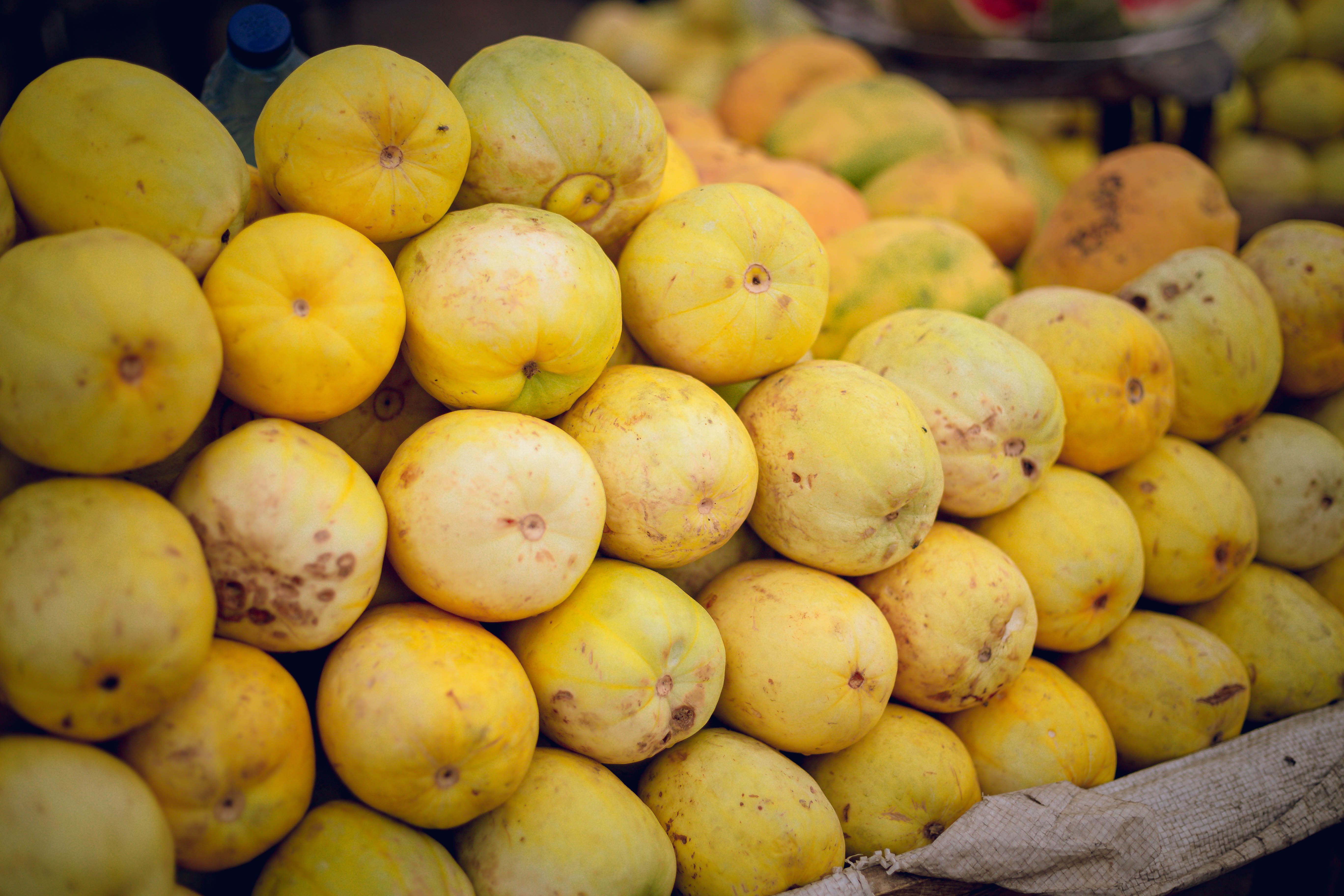 A vibrant display of yellow melons piled at an outdoor market stand, ripe and ready for sale.