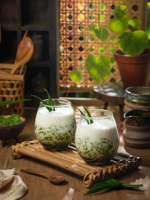Delicious traditional Indonesian cendol dessert served in bamboo cups amidst a rustic wooden backdrop.