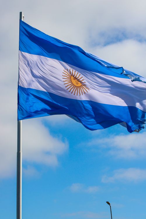 Free The national flag of Argentina waving against a bright blue sky, showcasing its vibrant colors. Stock Photo