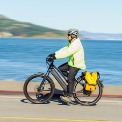 Cyclist in a hi-vis jacket riding an e-bike with a yellow and black roll-top pannier along the seafront