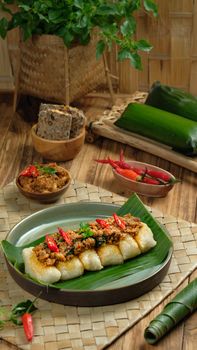Traditional Indonesian lemper with sambal, fresh spices, and herbs on a woven mat setting. - Fotografer Sidoarjo