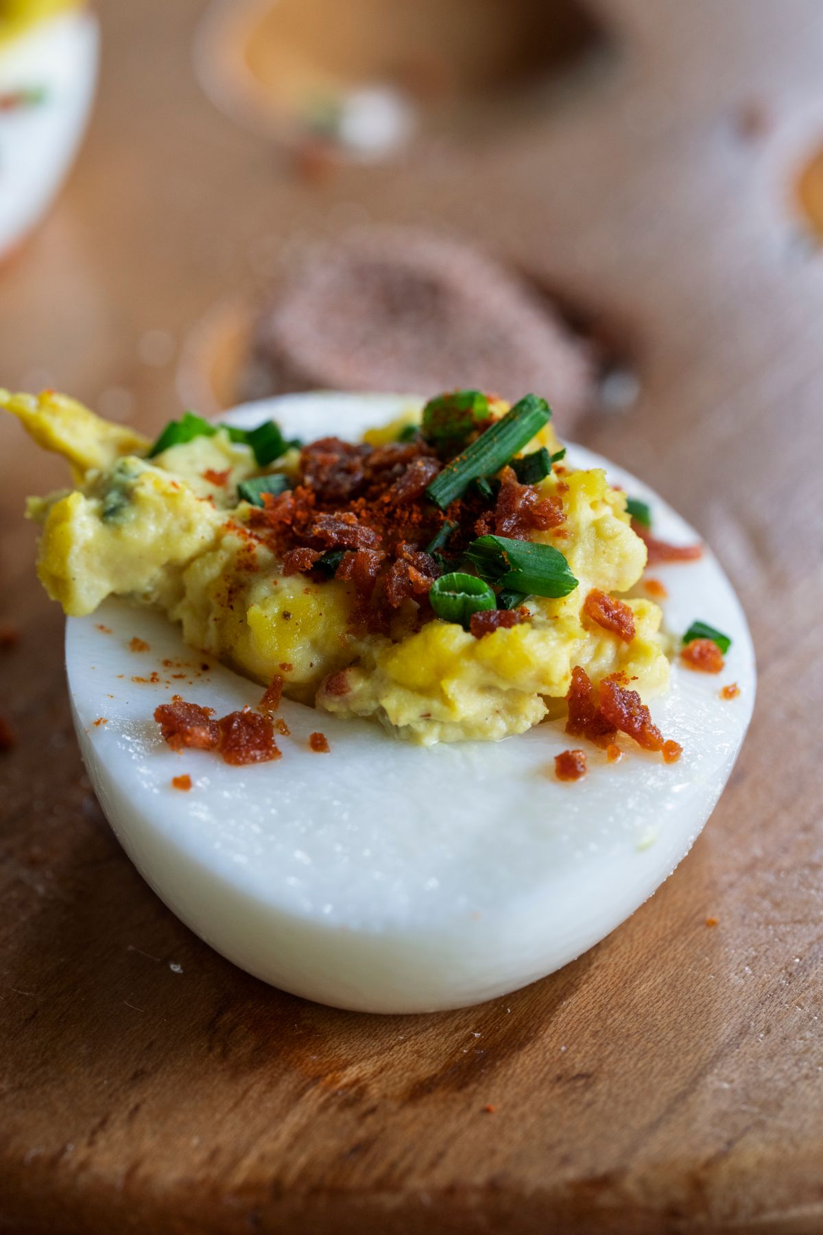 Deviled egg topped with chives and paprika on a wooden board