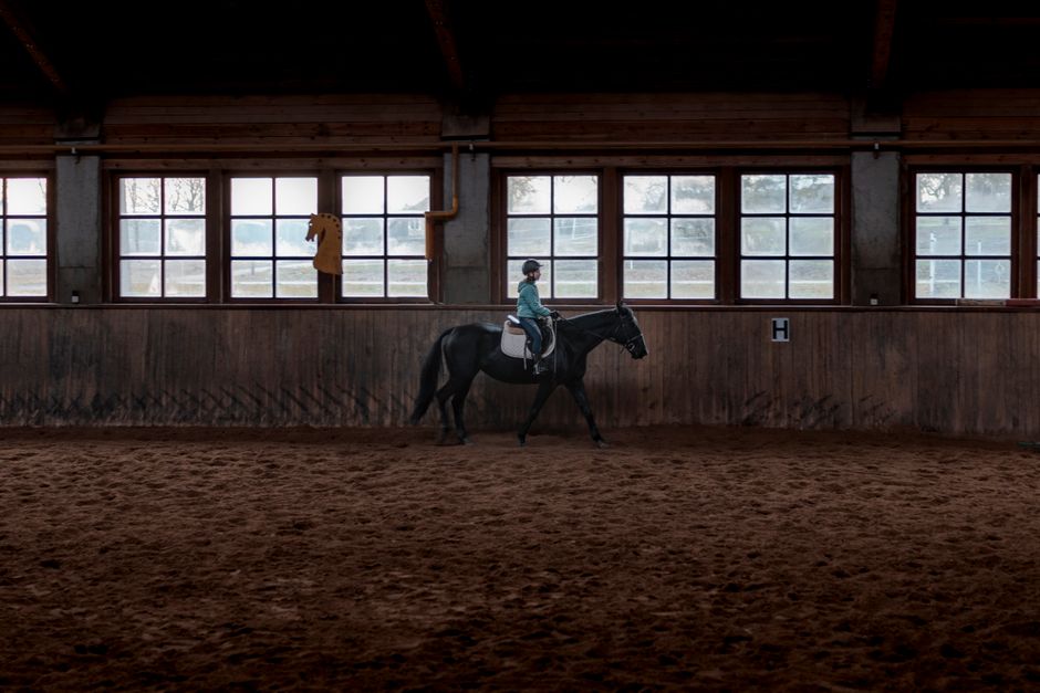Girl riding a black horse indoors, showcasing equestrian training in a stable setting.
