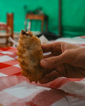 Close-up of a hand holding a traditional Argentine empanada with a blurred background. Iconic snack from Buenos Aires.