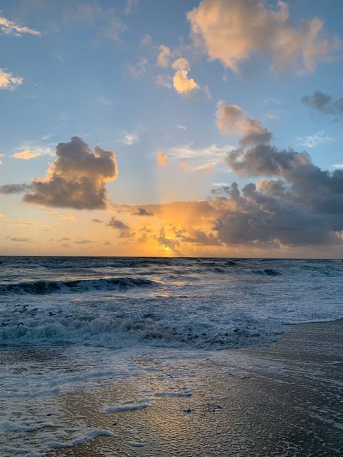 Free A breathtaking view of a serene ocean sunset with dramatic clouds and waves crashing on the shore. Stock Photo