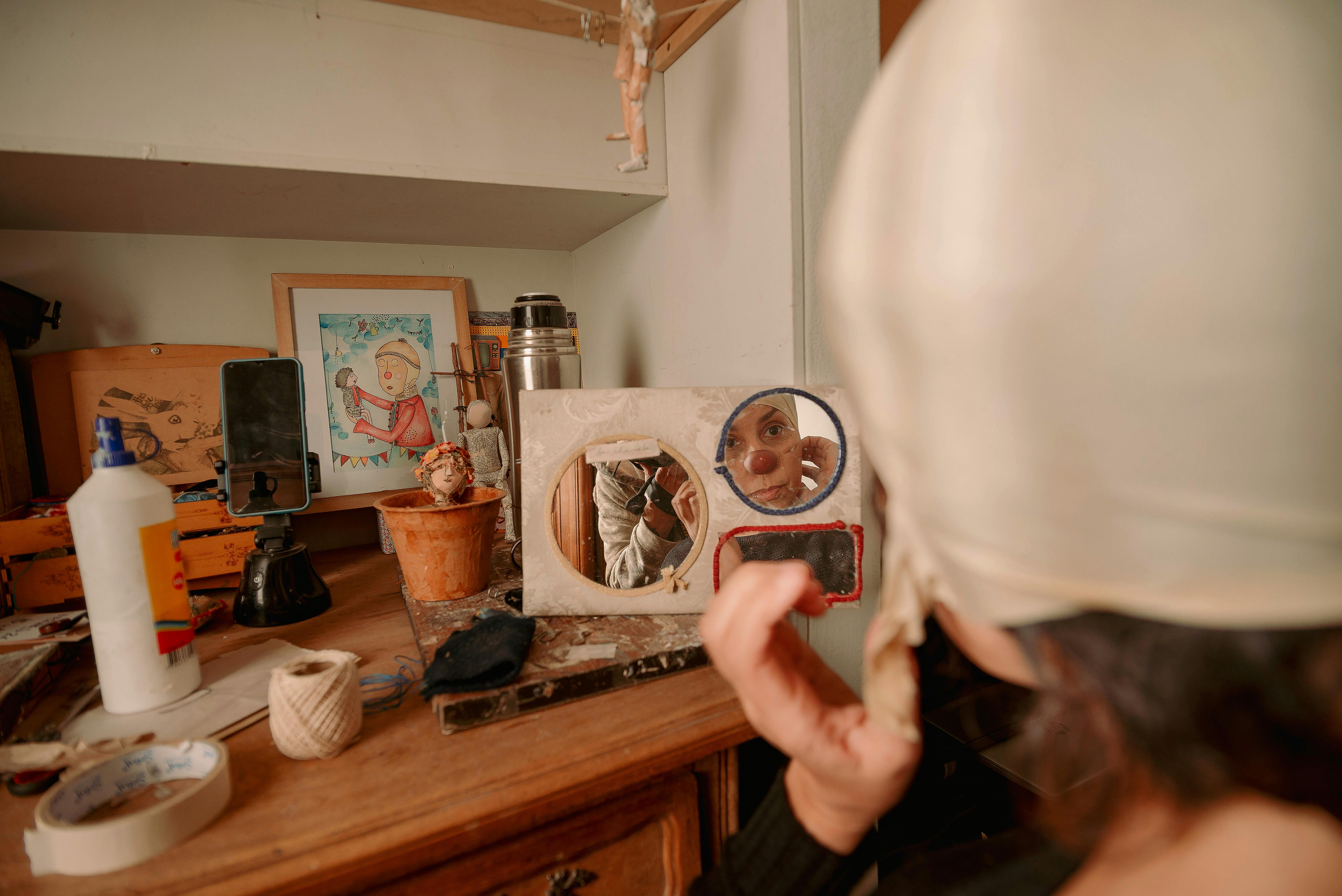 Artist wearing white cap applies makeup in cluttered workshop, reflecting creativity.