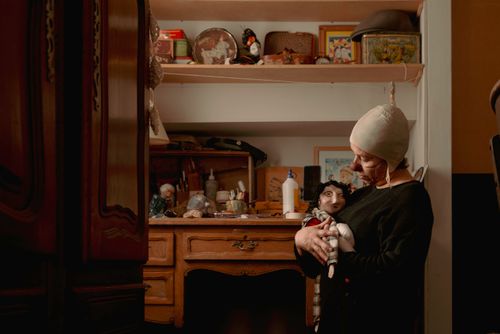 Free An artisan lovingly holds a puppet in a warm, vintage workspace filled with artistic materials. Stock Photo