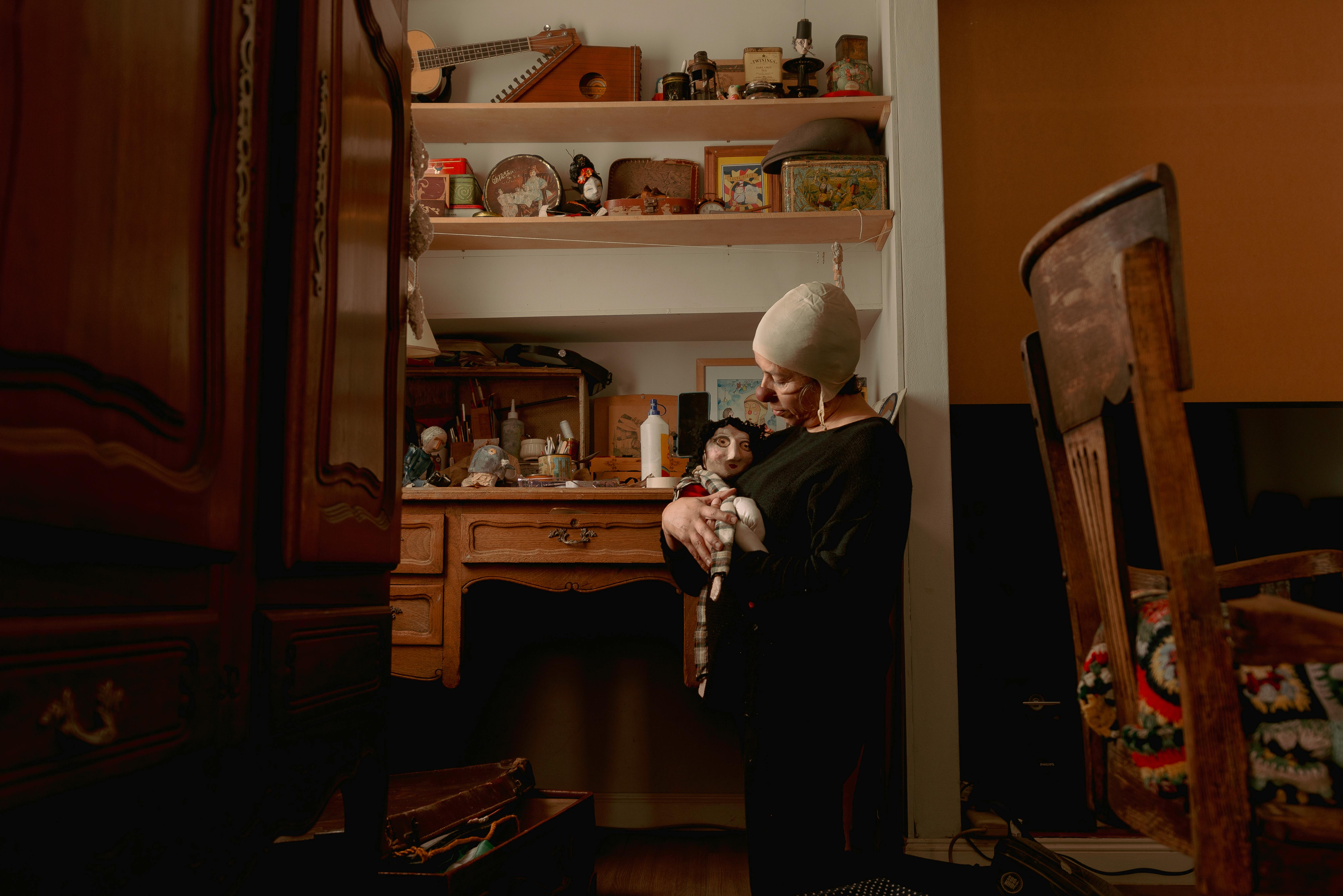A person holds a doll in a vintage styled room with wooden furniture and various collectibles.