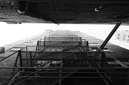 Free Dramatic black and white photograph of a fire escape viewed from below, creating a geometric pattern. Stock Photo