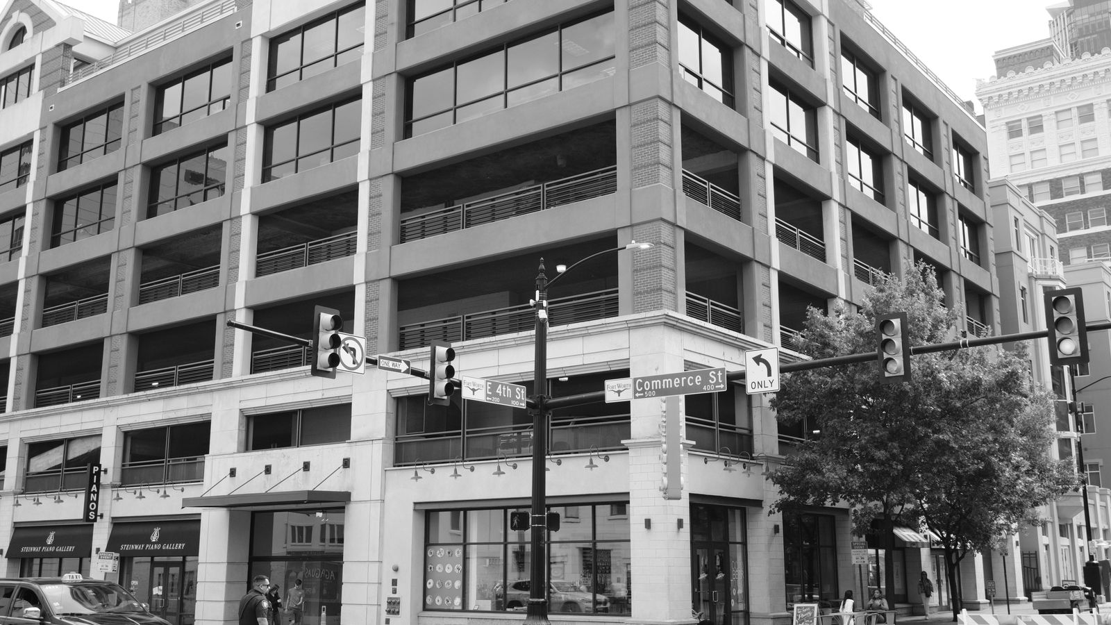 Black and white urban scene of downtown Fort Worth showing pedestrian, cars, and modern architecture.